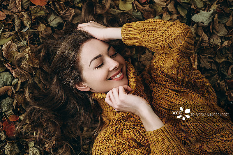 年轻女子躺在秋叶上。图片素材