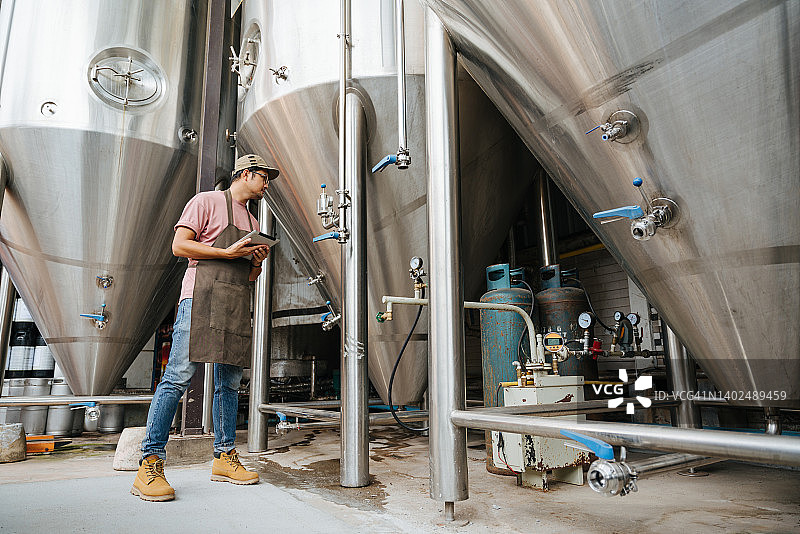 在仓库的精酿啤酒厂，一名酿酒师正在检查压力表。图片素材