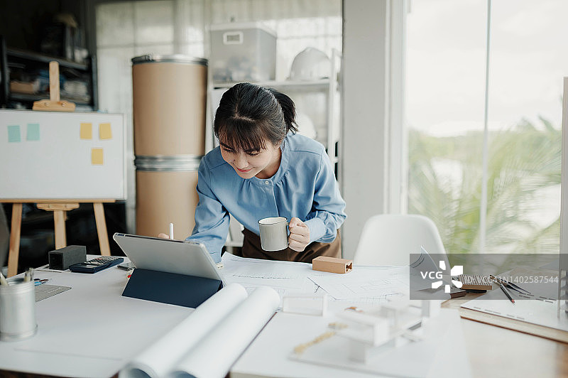 选择焦点，亚洲女性建筑师或工程师使用平板电脑绘制建筑内部的设计。亚洲女性建筑师或工程师坐在办公室里分析、设计项目。图片素材