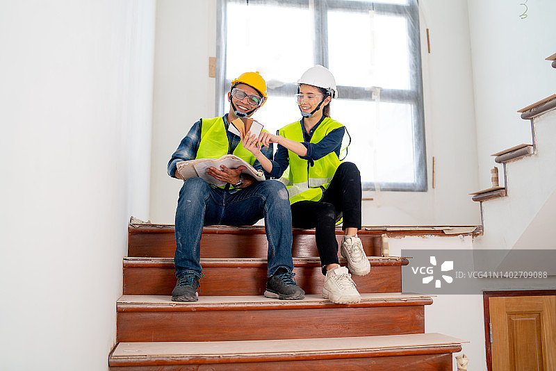 印度男工人和亚洲女工程师或经理在建筑工地的楼梯上一起工作图片素材