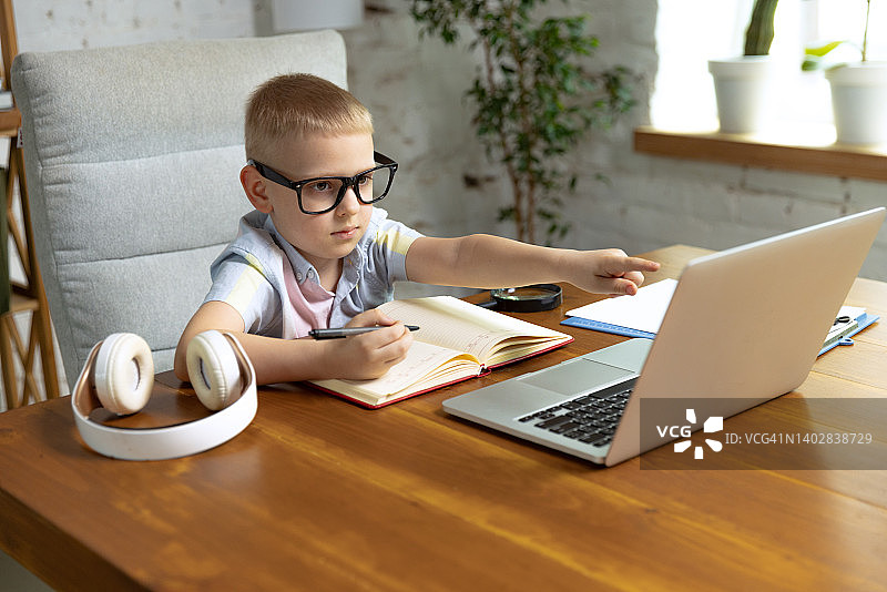 一个可爱的小男孩，学龄儿童在家里用笔记本电脑听在线课程。教育、童年、人、作业和学校观念。图片素材