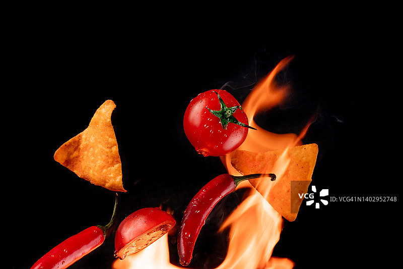 飞番茄，土豆，玉米片，红辣椒与火焰在黑色的背景图片素材