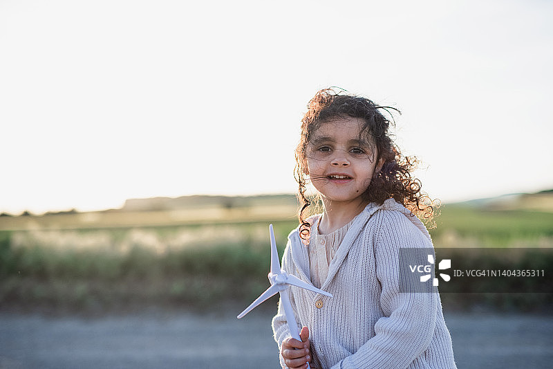 小女孩站在田野里，手里拿着风轮机模型。生态未来与可再生资源的概念。图片素材