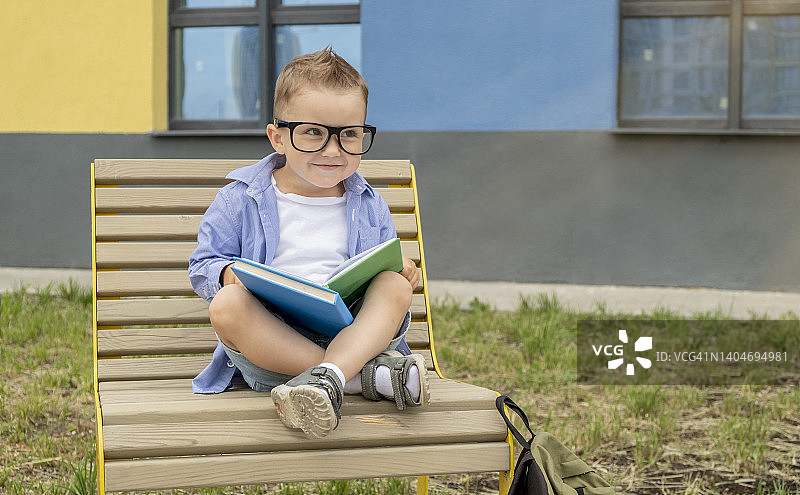 戴眼镜的搞笑男孩坐在长椅上看书。教育的概念图片素材