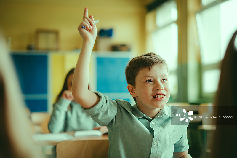 微笑的男生在教室里举手示意图片素材