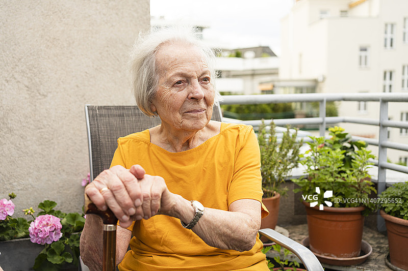 微笑的老妇人手持拐杖坐在阳台上图片素材