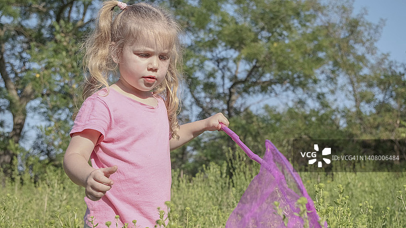 小女孩在城市公园玩高草的蝴蝶网。阳光灿烂的日子，可爱的小女孩在草地上玩空中捕虫网。图片素材