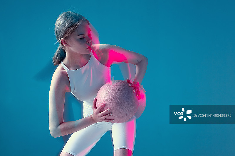 在粉红色的霓虹灯下，女篮球运动员拿着球移动。长时间的曝光。副本的空间。充满活力的体育锻炼图片素材