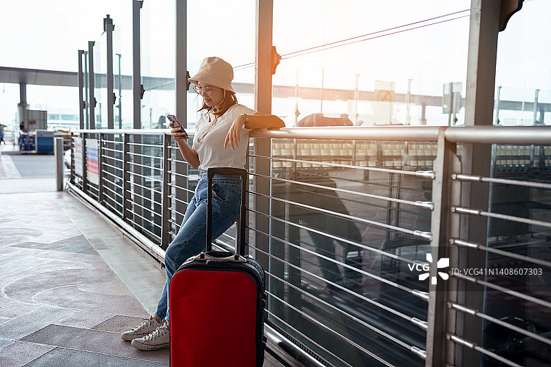 机场概念中的旅行箱旅行者。年轻的女孩用智能手机带着行李和乘客进行旅游旅行，预订机票，在国际度假，休息和放松。图片素材