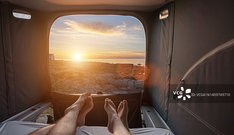 男女情侣睡在迷你面包车里，看着夏天日落的大海图片素材