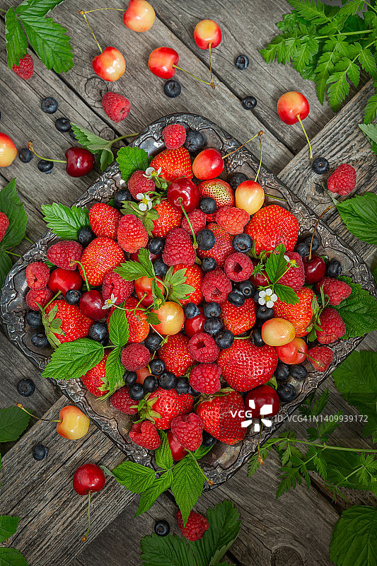 许多不同成熟的浆果草莓，覆盆子，蓝莓，樱桃，放在一个旧盘子和木制背景上。从上面的观点图片素材