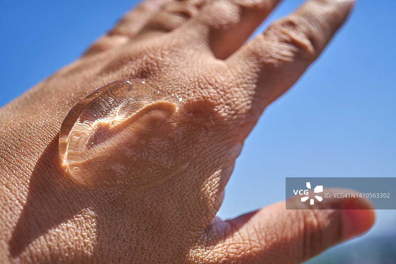 一滴化妆品凝胶在你的手上对着天空。这张照片可以作为防晒霜或夏季产品的示范。图片素材