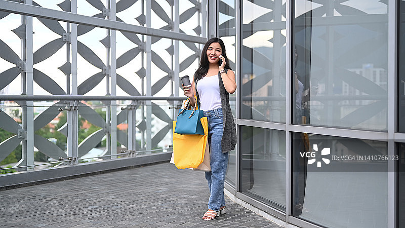 漂亮的亚洲女人携带购物袋和通话的手机。图片素材