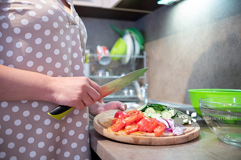 一位身穿棕色连衣裙的年轻女子在米褐色的厨房里烹制素食沙拉。图片素材