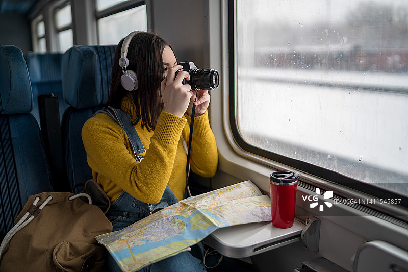 年轻女子享受火车旅行，用相机拍照。图片素材