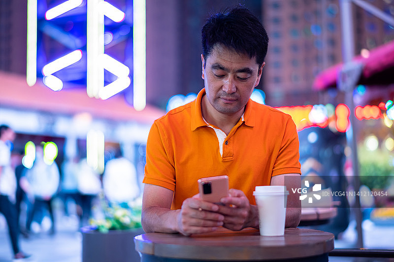 亚洲中年男子在城市街道上使用智能手机图片素材