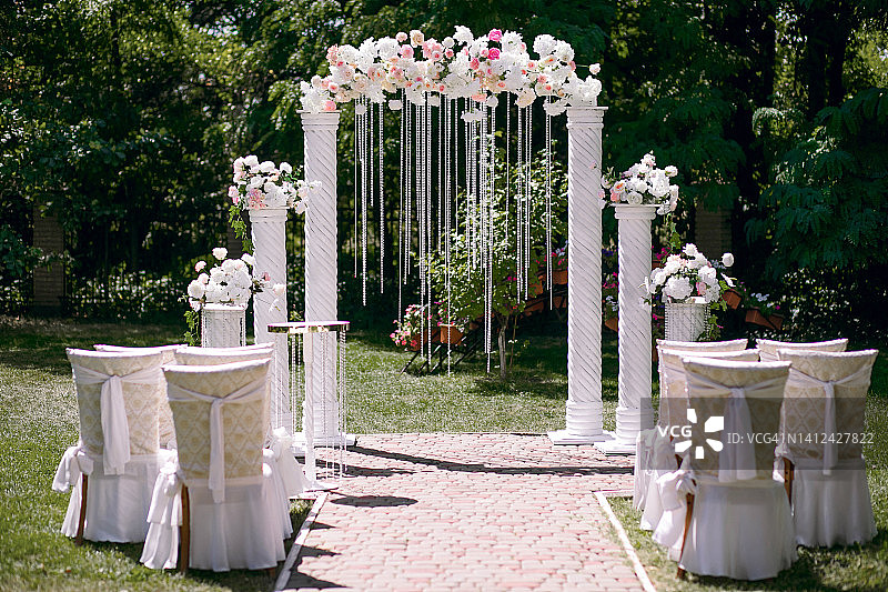 婚礼当天，白色的拱门为婚礼仪式和椅子的前夜，新娘和新郎退出图片素材