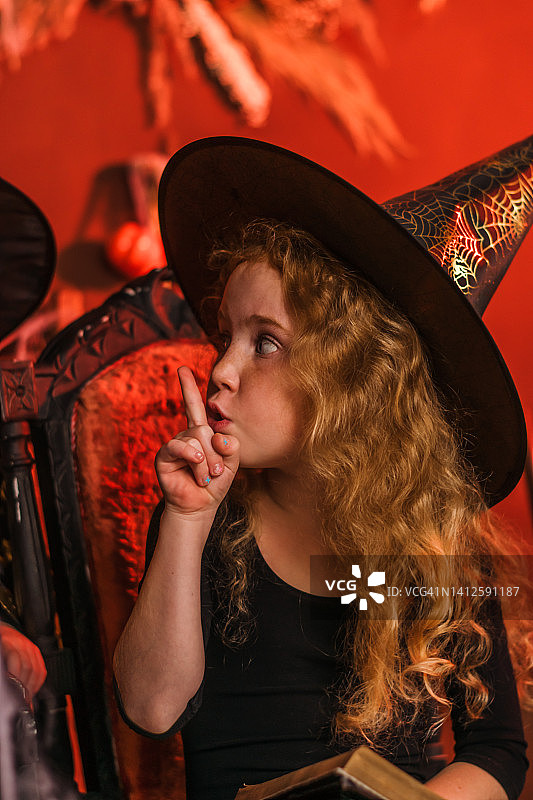 可爱的红头发女孩的肖像在黑女巫的服装和帽子的万圣节装饰。万圣节的概念。图片素材