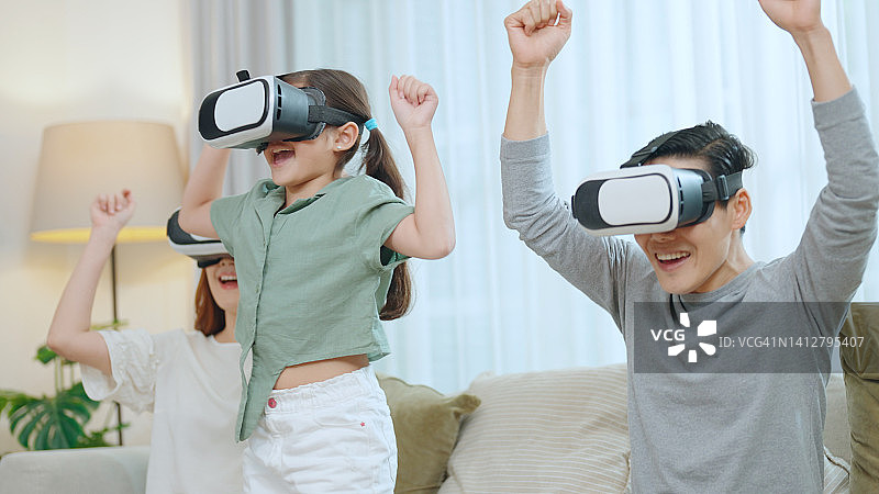 父母和女儿戴着虚拟现实眼镜玩电子游戏。图片素材