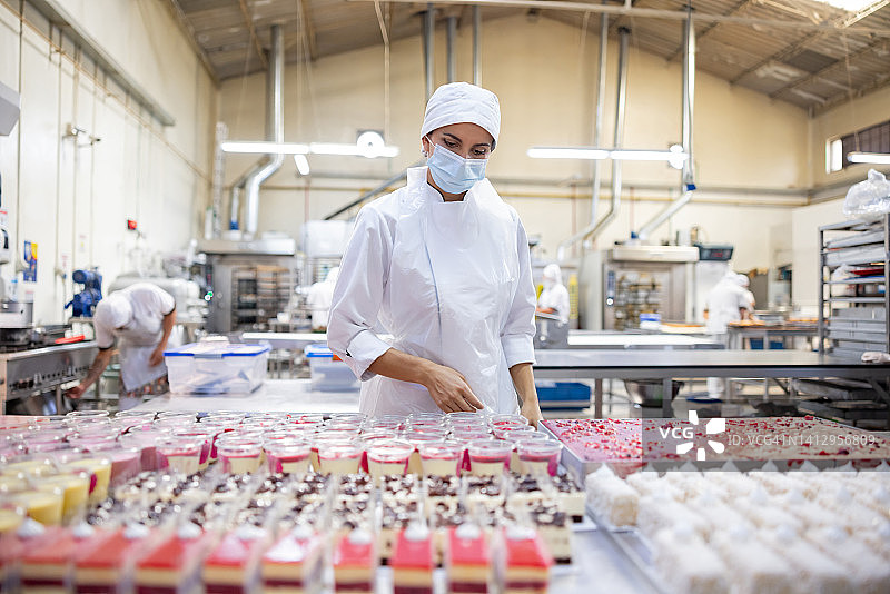 一位妇女在一家工业面包店工作，做一些高质量的甜点图片素材