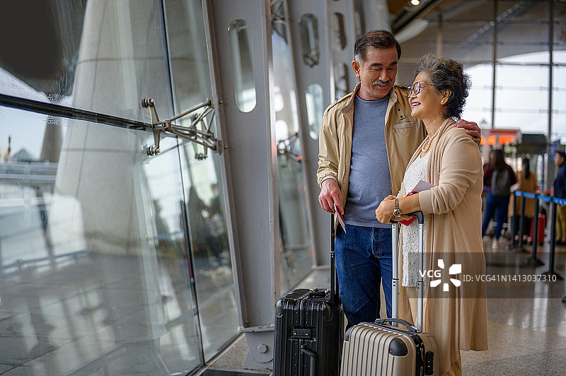在机场的到达出发大厅里，一对快乐的亚裔中国老夫妇望着窗外。图片素材