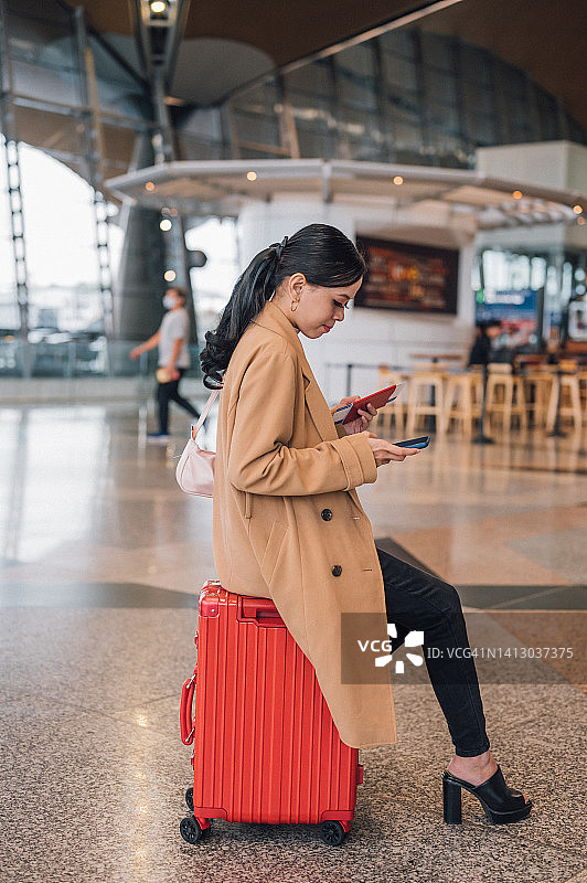 一名亚洲女商人在机场出境区坐在行李上用智能手机图片素材