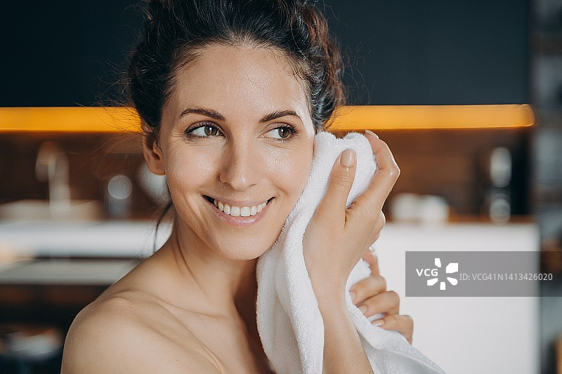 晚间美容日常及卫生。白种人幸福的女人洗脸后用毛巾擦脸。图片素材