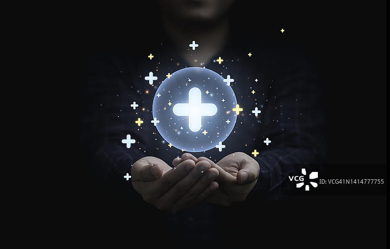 商人手持发光的加号图标，它象征着医疗保险和提供积极的思维心态的个人发展概念。图片素材