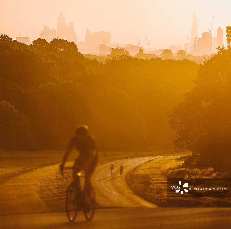 一个不知名的骑自行车的人在一个蜿蜒的道路在日出在伦敦公园-伦敦城市的背景图片素材