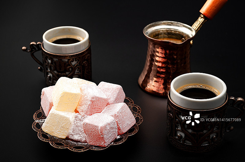 中东的好客和传统的沙漠概念主题与咖啡壶，小杯子和土耳其美食孤立的黑色背景图片素材
