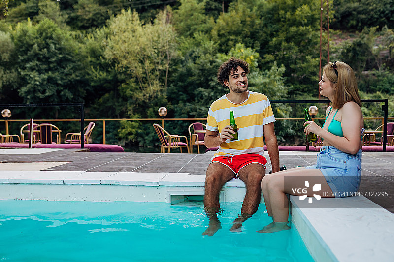 一个男人和一个女人坐在泳池边，喝着啤酒，享受着夏日的时光图片素材