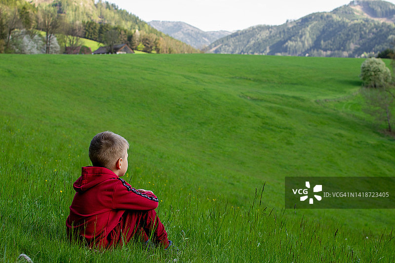 一个小男孩在绿色的草地上望着远方图片素材