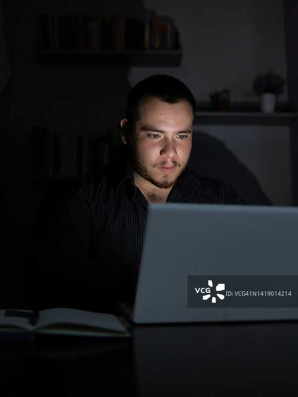 一个年轻人晚上在笔记本电脑前完成他的工作。图片素材