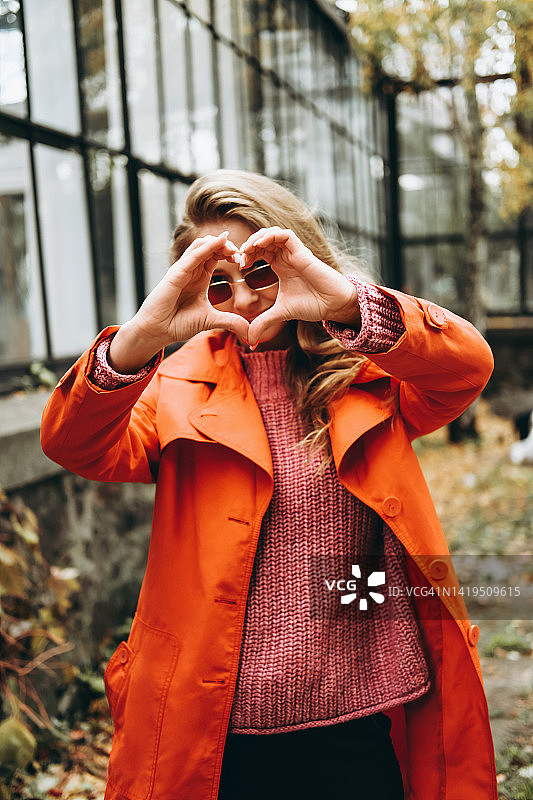 红衣少女在秋天的公园里露出爱心的标志。图片素材