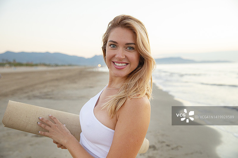 沙滩上，一个女人拿着瑜伽垫看着镜头图片素材