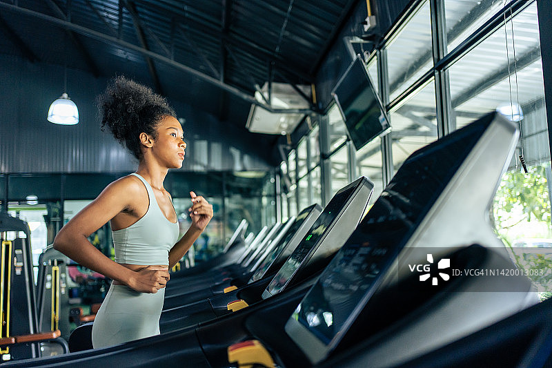 非洲裔美国女运动员在健身房的跑步机上锻炼身体。迷人的美丽运动员女孩练习锻炼，以保持肌肉和燃烧卡路里的健康福祉在健身体育场图片素材