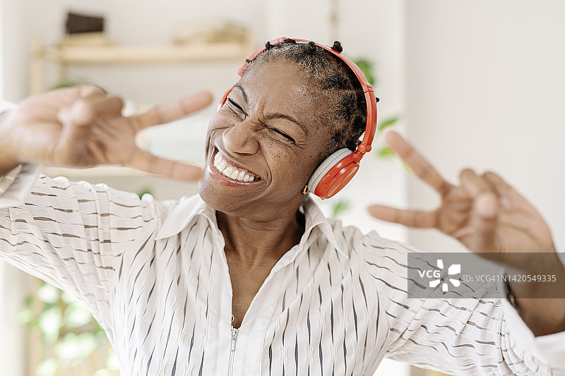 在家里戴着无线耳机显示和平手势的快乐女人图片素材