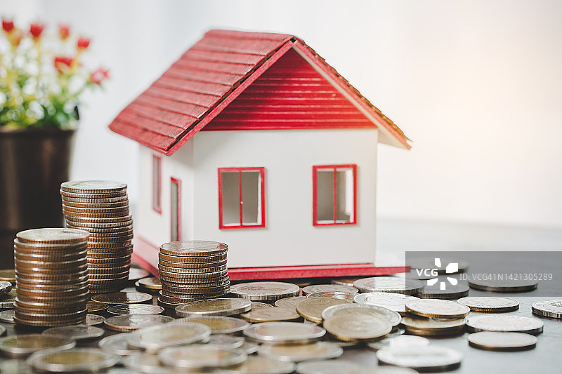 房子模型和硬币堆叠在模糊的桌子背景。住宅储蓄计划，贷款，投资，抵押，金融和银行关于房子的概念。图片素材