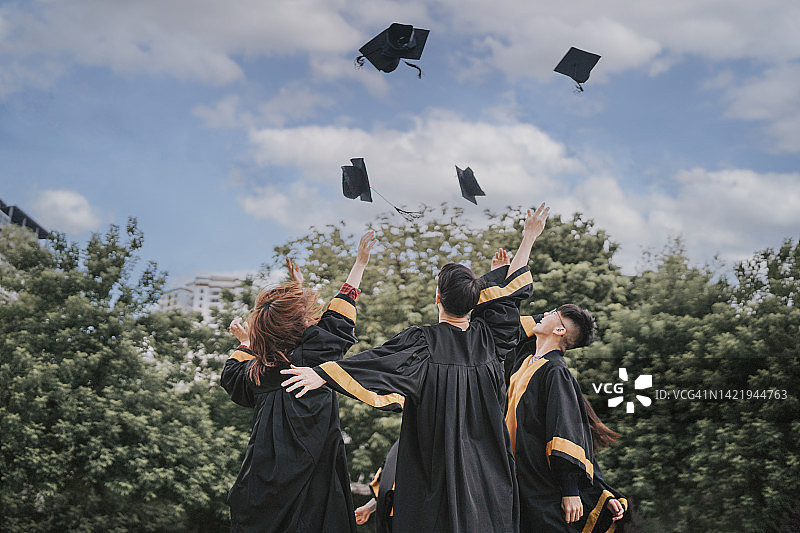 兴奋的亚洲学生在毕业日的传统中向空中投掷学位帽图片素材