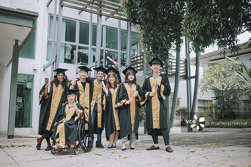 亚洲多元化的大学生们身穿毕业礼服，手握毕业证书，望着相机微笑着站在大学毕业典礼后合影留念图片素材