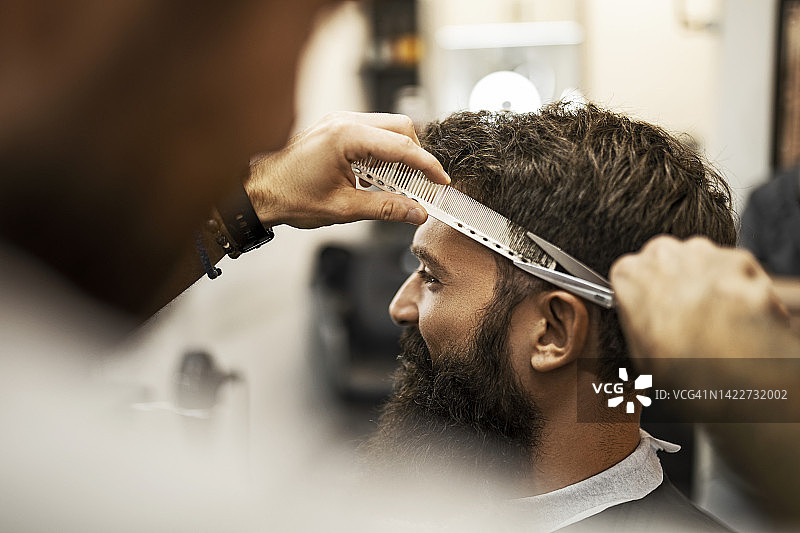 理发师在理发店里给一个大胡子男人理发图片素材