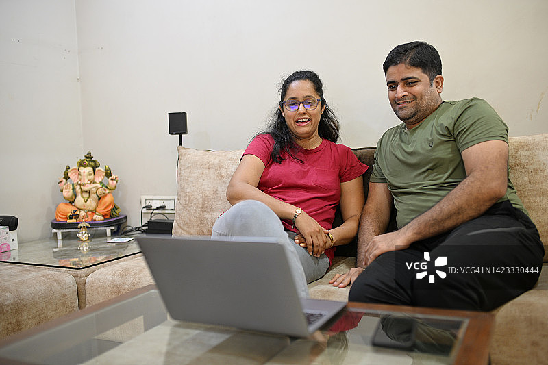 夫妻俩坐在客厅沙发上看笔记本电脑上的内容，面带微笑图片素材