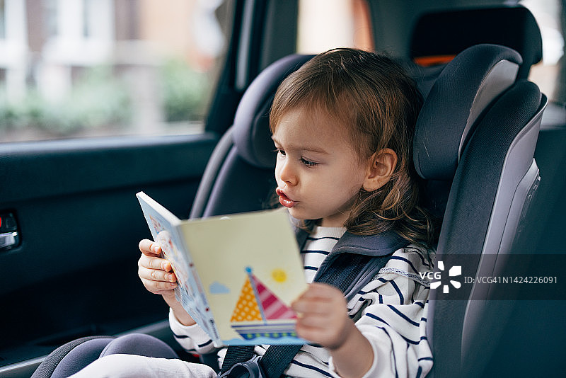 一个小女孩一边开车一边看书的画像图片素材