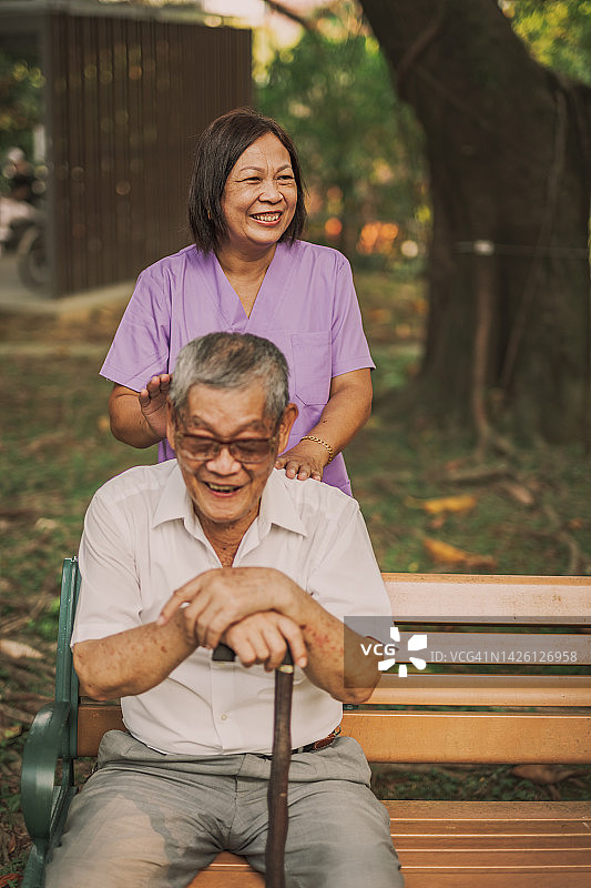 一位女护士愉快地为坐在公园长凳上的亚洲老人按摩图片素材