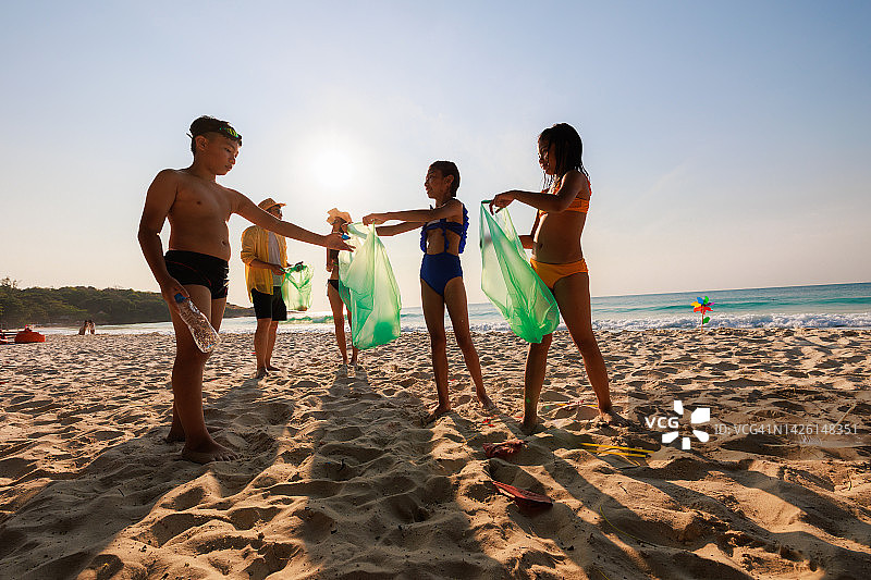 快乐的亚洲家庭清理海滩，把垃圾捡到垃圾袋里。志愿者与环保理念。图片素材