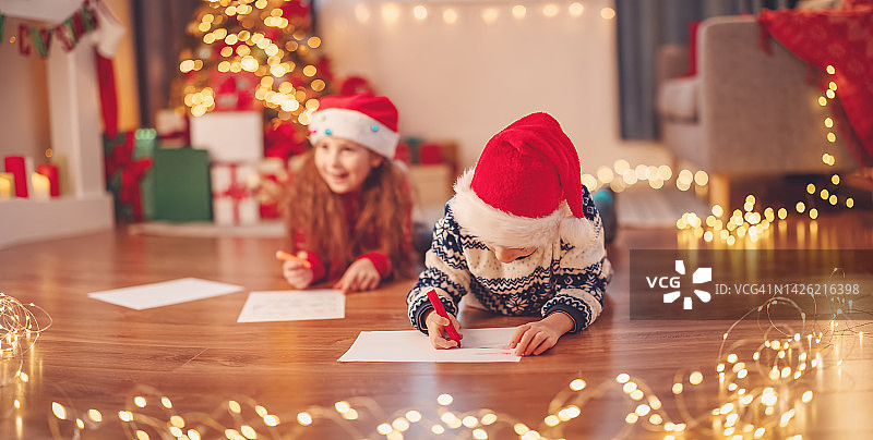 孩子们躺在室内的地板上给圣诞老人写信。图片素材