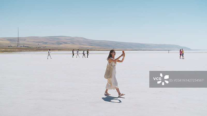在盐湖城，年轻的女旅行者走在白色的盐上，用她的智能手机拍照和视频Türkiye图片素材