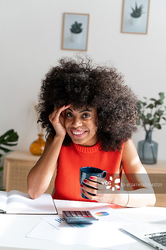 微笑的非裔美国妇女在家里拿着一杯咖啡工作图片素材