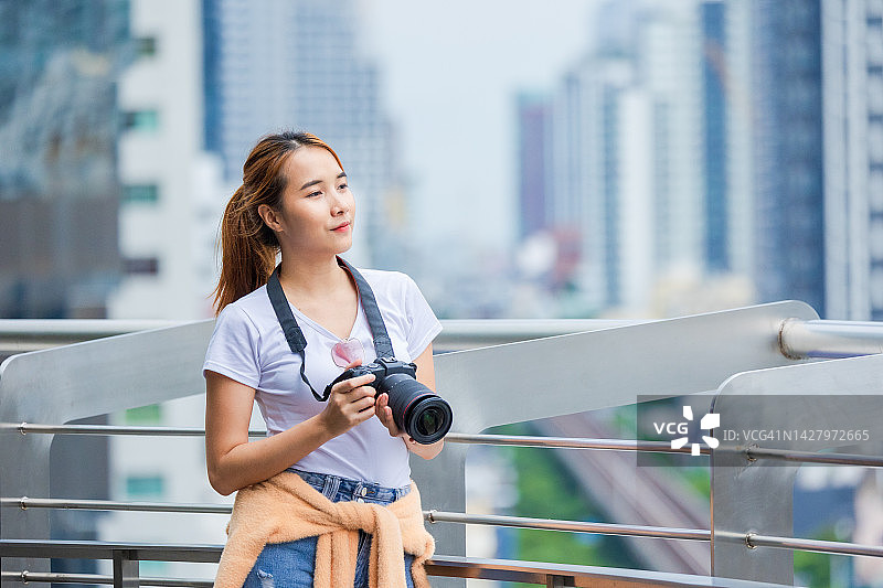 亚洲妇女在城市里用相机拍照。图片素材