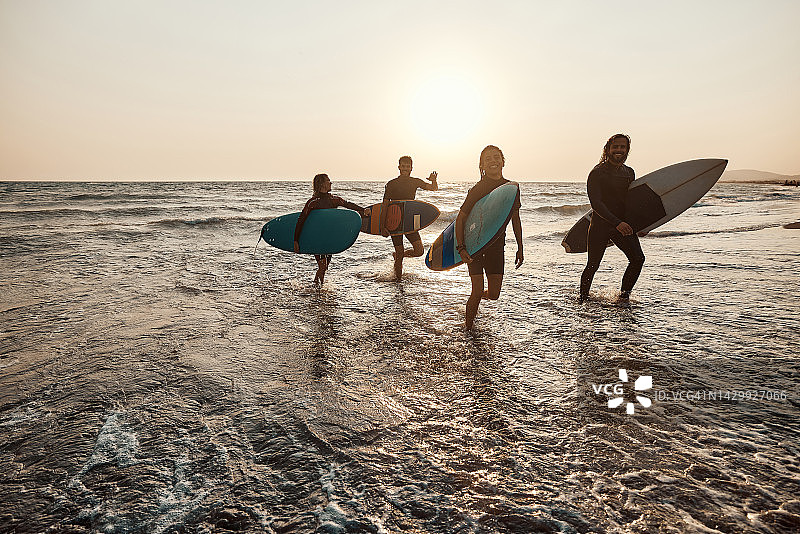 夕阳西下，快乐的冲浪者走出海面。图片素材